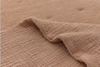 A close-up of a light brown, textured quilted blanket with a crinkled, wavy surface, showing a gently folded edge.