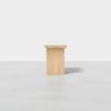 A minimalist wooden bench with a light-colored cushioned seat, set against a plain white background and placed on a smooth, light grey floor.