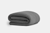 A neatly folded, dark gray textured blanket is placed on a plain, light-colored surface with a white background.