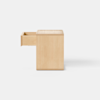 A square wooden box with a light, natural finish sits on a smooth, light gray floor against a plain white background.