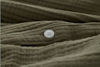 A close-up of an olive green, textured fabric with a single white, four-hole button sewn onto it. The fabric appears soft and slightly wrinkled.