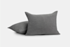 Two gray textured pillows are shown against a plain white background, with one pillow standing upright and the other lying flat behind it.