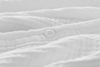 A close-up of a white button sewn onto soft, textured white fabric with gentle folds and ripples. The overall appearance is clean and minimalistic.