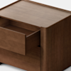 A simple, modern wooden nightstand with a natural finish, featuring one drawer partially open. The background is plain and light, highlighting the clean lines and minimalist design of the nightstand.