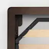 Close-up of a wooden bed frame corner showing a dark brown outer edge, light wood slats, and black metal supports, against a plain white wall background.