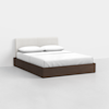 A modern platform bed with a dark wooden frame, white upholstered headboard, and neatly made white bedding with two pillows, set in a minimal, light-colored room.