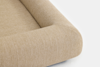 Close-up of the corner of a beige upholstered sofa or couch with rounded edges, showing the textured woven fabric and smooth, modern design against a plain white background.