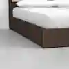 A close-up of a modern bed with a dark wooden frame, white sheets, and two white pillows, placed on a light gray floor against a plain white wall.