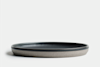 A round, flat, ceramic plate with a matte gray exterior and a smooth, dark interior, set against a plain white background.