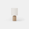 Table lamp with a cylindrical tan base and a neutral fabric drum shade.