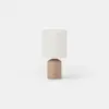 Table lamp with a cylindrical tan base and a neutral fabric drum shade.