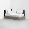 A modern daybed with a light wood base, dark upholstered backrest, and four white pillows is placed in a minimal, empty room with white walls and a light gray floor.