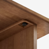 Close-up view of the underside of a wooden tabletop with a recessed, round black screw or fastener securing the table leg to the top, against a plain white background.