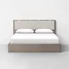 A modern platform bed with a light wood frame, beige upholstered headboard, white bedding, and two white pillows, set against a plain white wall and gray floor.