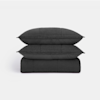 Two black pillows are stacked on top of a folded black quilt, all showing a quilted pattern, against a plain white background.