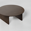 A round, dark wooden coffee table with three thick, flat legs on a light gray surface.