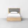 A minimalist wooden bed with a light wood frame, gray cushioned headboard, and white bedding, set against a plain white wall and gray floor.
