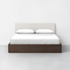 A modern bed with a white upholstered headboard, white bedding, and two pillows, set on a dark wooden frame against a plain white wall and gray floor.