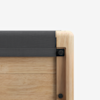 Close-up of the corner of a light wood frame with visible grain, featuring a black fabric cushion and black hardware against a white background.