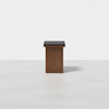 A modern wooden stool with a rectangular base and a black cushioned seat, displayed on a light, minimalist background.