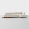 A modern, L-shaped sectional sofa with light beige upholstery and a wooden base, placed on a smooth, light gray floor against a plain white background.
