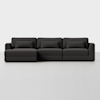 A modern, dark gray sectional sofa with three seat cushions, three back cushions, and three rectangular pillows, set against a plain white background. The left side features a chaise lounge extension.