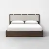 A modern bed with a dark wood frame, a light upholstered headboard, white bedding, and two white pillows, set against a plain white wall and light gray floor.