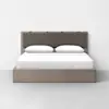 A modern wooden bed with a brown upholstered headboard, neatly made with white bedding and two white pillows, set against a plain white wall on a light gray floor.
