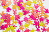 Scattered jigsaw puzzle pieces in bright colors, including pink, orange, and yellow, lying on a white surface. None of the pieces are connected.