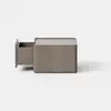 A simple, square, brown wooden box sits on a smooth, light gray surface against a plain white background.