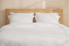 A close-up of neatly folded white bed sheets and pillowcases stacked on top of each other against a plain white background.