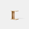 A minimalist, light wood side table shaped like an uppercase I, with a flat top and base connected by a vertical support, set against a plain, light gray background.