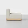 A modern armless beige upholstered chair with a wooden base, shown from the side against a plain white background.