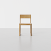 A simple, modern wooden chair with a straight back and square seat, placed on a light gray floor against a plain white background.