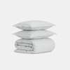 Two light gray pillows are stacked on top of a neatly folded matching comforter, all set against a plain white background.