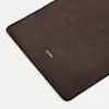 A close-up of a dark brown suede mat with rounded corners, featuring the word THUMA printed in small white letters near the edge. The surface appears soft and velvety.