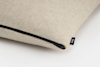 A close-up of a light beige pillow with a visible black zipper along the seam and a small black tag labeled THUMA on the side.