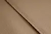 Close-up of beige textured leather with a visible seam running diagonally across the image, showing fine grain and neat stitching.