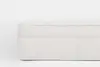 A close-up side view of a mattress with a white, quilted cover and a soft, padded top, set against a plain white background.