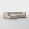 A modern, light beige L-shaped sectional sofa with low backs and wide seats, set on a wooden base, positioned on a smooth, light-colored floor against a plain white background.