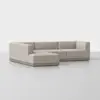 A modern, light beige L-shaped sectional sofa with low backs and wide seats, set on a wooden base, positioned on a smooth, light-colored floor against a plain white background.