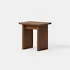 A small, modern wooden side table with a rectangular top and two thick, straight legs on each side, connected by a horizontal support panel. The wood has a warm, medium-brown finish and the background is plain white.