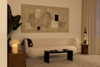 A modern living room with a curved beige sofa, abstract wall art, a black coffee table, a wooden side table with a small plant, a lit table lamp, and neutral-colored curtains. The lighting is warm and cozy.