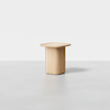 A minimalist wooden side table with a square top and rounded edges, featuring a solid, cylindrical base, photographed against a plain white background.