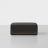 A modern, rectangular black ottoman with a dark wooden base sits on a light gray floor against a plain white background.