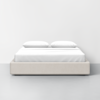 A modern, minimalist bed with a light beige upholstered base, white sheets, and two white pillows, set against a plain white wall and gray floor.