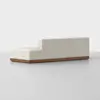 A modern, minimalist beige sectional sofa with clean lines and a low wooden base, set against a plain light background. The sofa has one arm and backrest at different heights.