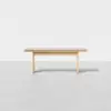 A minimalist wooden bench with a light finish, featuring a flat rectangular seat and four simple legs, set against a plain white background.