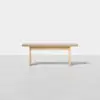 A minimalist wooden bench with a light finish, featuring a flat rectangular seat and four simple legs, set against a plain white background.