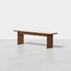 A minimalist wooden bench with a light-colored cushioned seat, two rectangular legs, and a simple, modern design, set against a plain white background.